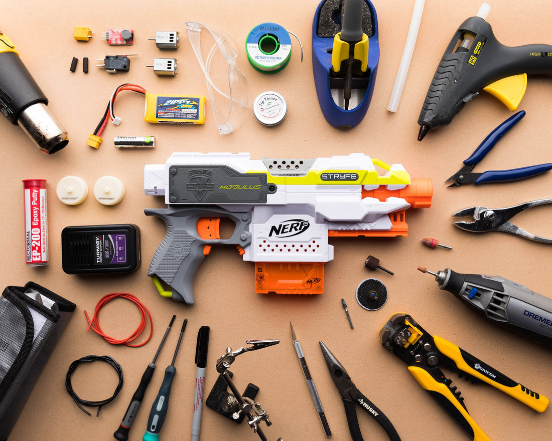 Nerf blaster modding tools and accessories arranged around a Nerf Stryfe blaster